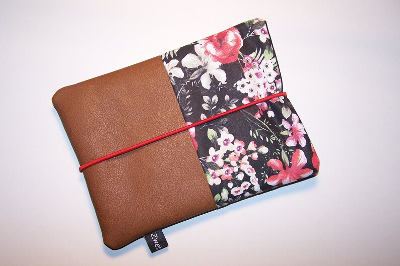 May include: A brown leather and floral fabric pouch with a red elastic band closure. The pouch has a black label with the word "Zwei" on it.