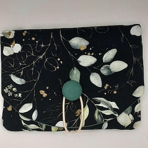 Könnte beinhalten: Eine schwarze Stofftasche mit grünem Knopfverschluss und einem weißen und goldenen Blumenmuster.