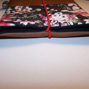 May include: A brown leather notebook with a black floral fabric cover and a red elastic closure.