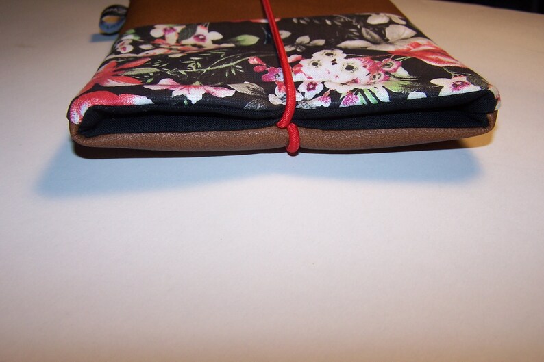 May include: A brown leather notebook with a black floral fabric cover and a red elastic closure.