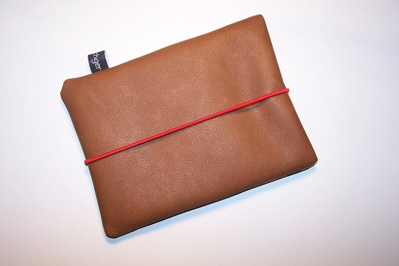May include: A brown leather pouch with a red elastic band. The pouch has a small black label with the word "Finger" printed on it.