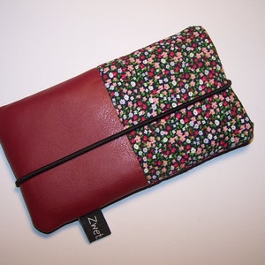 Könnte beinhalten: Eine bordeauxrote Leder-Handyhülle mit einem floralen Stofffutter und einem schwarzen Gummibandverschluss. Die Hülle hat ein kleines schwarzes Etikett mit dem Wort "Zwet" darauf.