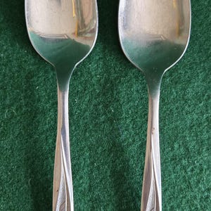 May include: Two silver spoons with floral designs on the handles. The spoons are on a green surface.