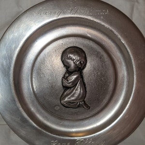 May include: A silver metal plate with a raised image of a child praying. The plate has the words "Merry Christmas" and "Love Tiffany 1977" inscribed on it.