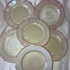 May include: Set of six white dinner plates with a pink and iridescent glaze. The plates have a scalloped edge and a gold rim.