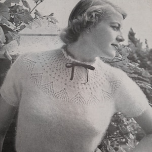 May include: A white knitted sweater with a delicate lace pattern around the neckline. The sweater has short sleeves and a fitted silhouette. The text "TO FIT 34 INCH BUST-51" is printed at the top of the image.