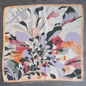 May include: A silk scarf with a floral design in shades of pink, orange, purple, and gray. The scarf has a peach-colored border.