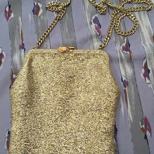 May include: A gold-coloured, textured evening bag with a chain strap. The bag has a rectangular shape with a clasp closure. The chain is also gold-coloured.
