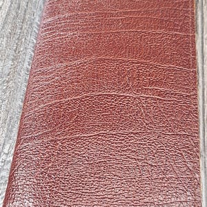May include: A rectangular, folded brown wallet featuring a textured, embossed surface pattern that mimics the appearance of animal skin. The wallet is constructed with visible stitching along the edges and maintains a slim, vertical orientation.