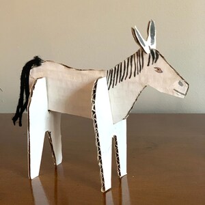 May include: A cardboard donkey sculpture with black and white stripes, white legs, and a black tail. The donkey is painted with brown and white details.