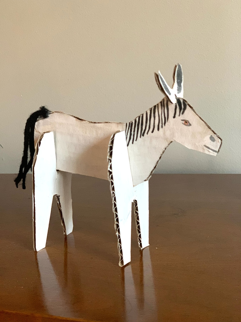May include: A cardboard donkey sculpture with black and white stripes, white legs, and a black tail. The donkey is painted with brown and white details.