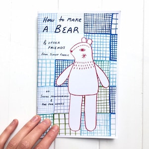 May include: A handmade booklet titled "How to Make a Bear & Other Friends From Scrap Fabric." The cover features a white bear illustration with red accents, set against a blue and green grid pattern. The author's name is also visible.