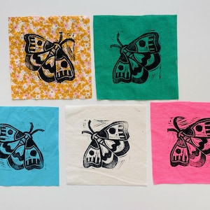 May include: Five square fabric pieces, each featuring a black and yellow moth linocut print. The backgrounds are various colors: floral yellow, green, blue, white, and pink. The moth design is consistent across all pieces.