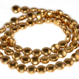 May include: A strand of gold-toned round beads, each bead has a slightly flattened shape. The beads are strung on a clear thread.