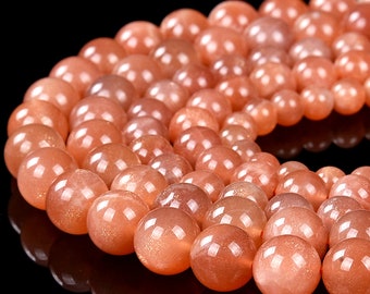 May include: A strand of round, orange sunstone beads. The beads are smooth and polished, with a slight shimmer.