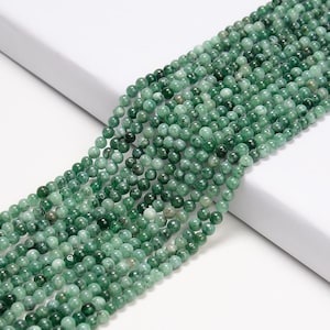 May include: A strand of green jade beads, each bead is round and smooth. The beads are strung on a clear thread and are ready to be used for jewelry making.