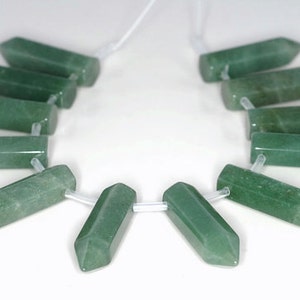 May include: A strand of 10 green gemstone beads, each shaped like a long, pointed, rectangular prism. The beads are strung on a clear elastic cord.