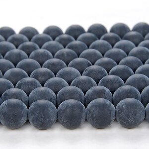 May include: A close-up of a group of dark gray round beads arranged in a grid pattern. The beads are smooth and have a matte finish.