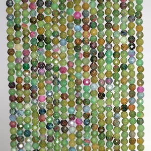 May include: Close-up of strands of gemstone beads. The beads are a mix of colours, including green, pink, and brown. The beads are round and faceted, creating a textured surface. The beads are strung together in vertical rows.