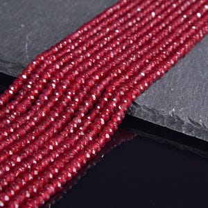 May include: Close-up of multiple strands of faceted, deep red beads. The beads are small and evenly sized, with a sparkling, reflective surface. The strands are arranged closely together, creating a rich, textured appearance. Ideal for jewelry making.