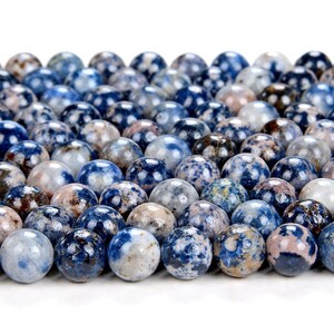 K&ouml;nnte beinhalten: Nahaufnahme einer Sammlung runder, blau, wei&szlig; und braun gesprenkelter Perlen. Die Perlen sind aus Naturstein und haben eine marmorierte Optik.