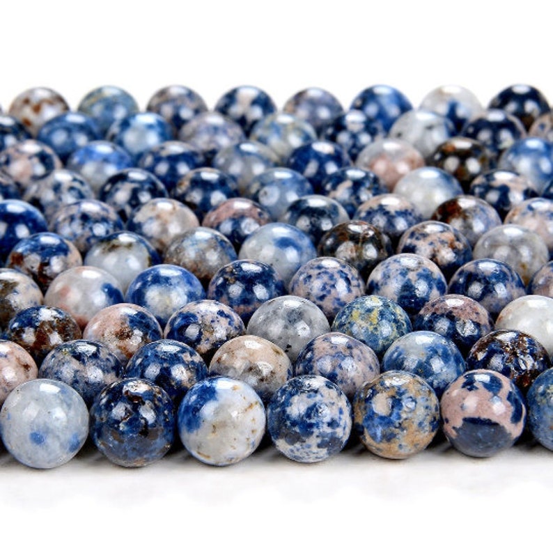 K&ouml;nnte beinhalten: Nahaufnahme einer Sammlung runder, blau, wei&szlig; und braun gesprenkelter Perlen. Die Perlen sind aus Naturstein und haben eine marmorierte Optik.