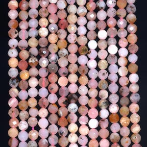 Puede incluir: Una hebra de cuentas de ópalo rosa facetadas. Las cuentas son una mezcla de rosa claro y oscuro con algunas inclusiones marrones y blancas. Las cuentas están enhebradas en un cordón elástico transparente.