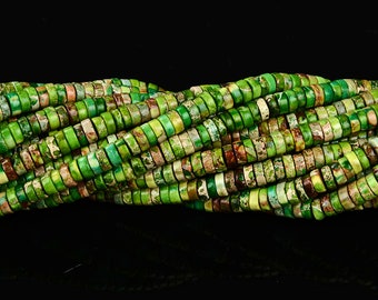 Può includere: Una collana di perline di diaspro verde, marrone e bianco. Le perline sono rotonde e hanno una finitura liscia e lucida. Sono infilate su un filo elastico trasparente.