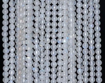 May include: Strands of round, translucent, white moonstone beads. The beads are strung together, creating a flowing, textured appearance. The beads have a subtle iridescence, with hints of blue and rainbow colors. The background is black.