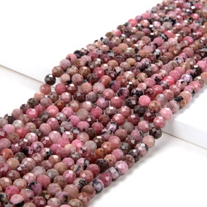 Puede incluir: Una hebra de cuentas redondas facetadas de color rosa y gris hechas de piedra preciosa de rodonita. Las cuentas están enhebradas en un hilo transparente y están listas para ser utilizadas en la elaboración de joyas.