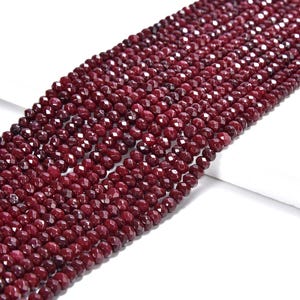 May include: A strand of deep red faceted gemstone beads. The beads are round and have a smooth, polished finish.