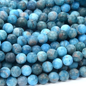 May include: A strand of blue apatite beads. The beads are round and have a smooth, polished finish. They are a light blue color with some darker blue and white streaks.