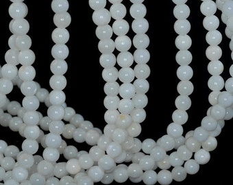 May include: A strand of white round beads made from natural shell. The beads are smooth and have a slight iridescent sheen.