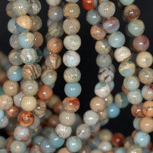 May include: A strand of light blue, brown, and white gemstone beads. The beads are round and have a mottled appearance.