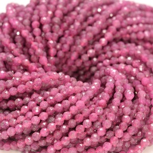 May include: A strand of pink faceted gemstone beads. The beads are round and have a slightly rough texture.