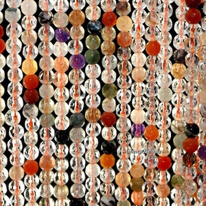 May include: A strand of faceted clear quartz beads with inclusions of various colors, including red, orange, yellow, green, blue, and purple. The beads are strung on a thin, red thread.