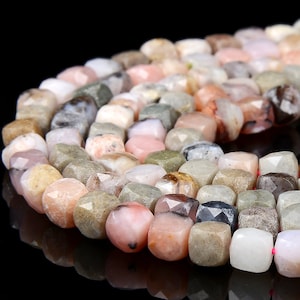 Puede incluir: Una hebra de cuentas de piedra preciosa de forma cuadrada y facetada en tonos rosa, marrón y gris. Las cuentas están enhebradas en un cordón elástico transparente.