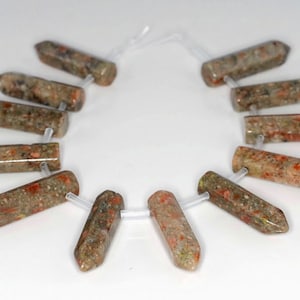 May include: A strand of 12 brown, green, and orange gemstone beads with a pointed tip. The beads are strung on a clear elastic cord.