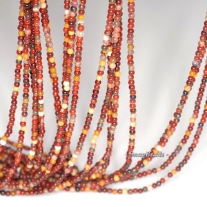 May include: A strand of red, brown, and cream colored gemstone beads. The beads are small and round, and they are strung on a clear thread. The beads are all different sizes and shapes, and they have a natural, rustic look.