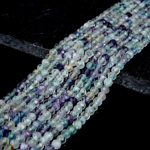 May include: A strand of faceted gemstone beads in shades of green, blue, and purple. The beads are round and have a smooth, polished finish.