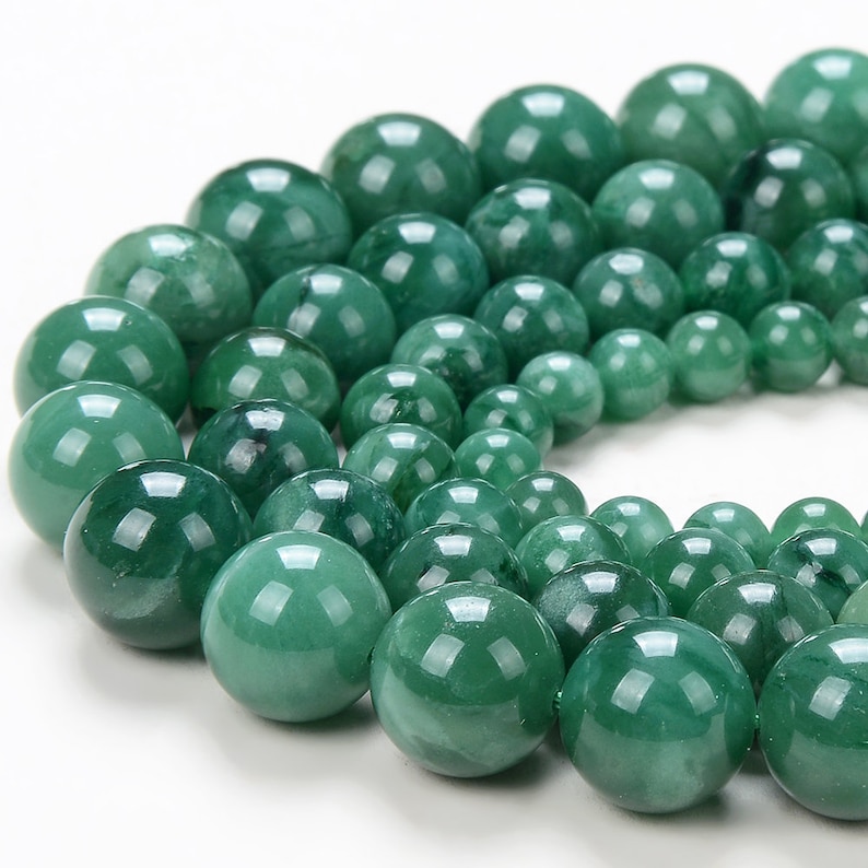 May include: A strand of round, green jade beads. The beads are smooth and polished, with a slight variation in color and texture. The beads are arranged in a circle, with the largest beads in the center and the smaller beads on the outside.