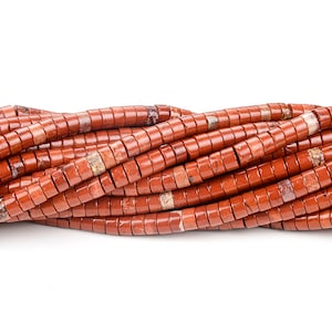 May include: A strand of red jasper beads, each bead is a cylinder with a slightly rounded edge. The beads are arranged in a wavy pattern.