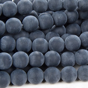 May include: A close-up of a strand of dark gray matte round beads. The beads are smooth and have a slightly textured surface.