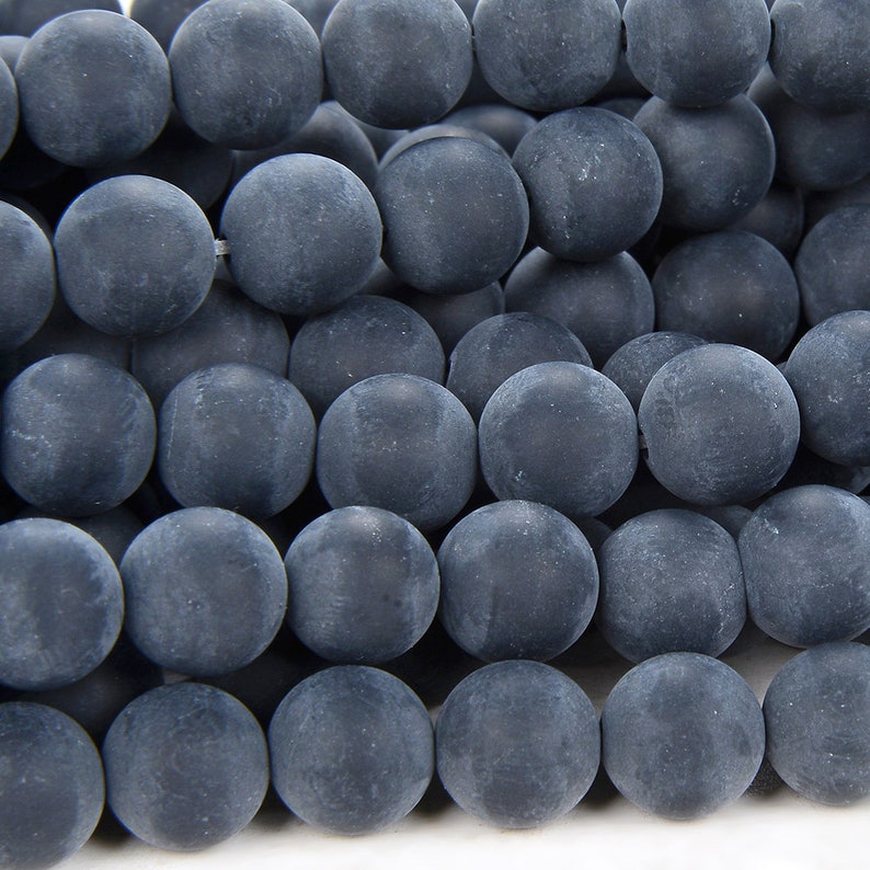 May include: A close-up of a strand of dark gray matte round beads. The beads are smooth and have a slightly textured surface.