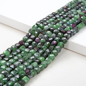 May include: A strand of green and black faceted gemstone beads. The beads are square shaped and have a slightly irregular, rough texture.