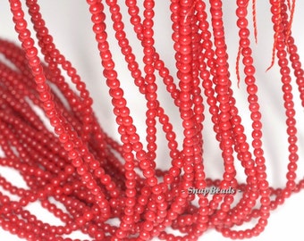 May include: A strand of bright red coral beads. The beads are small and round, and they are strung on a thin thread. The beads are all the same size and shape, and they are evenly spaced.