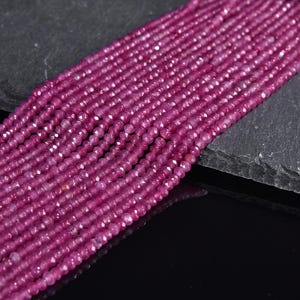 May include: A strand of pink faceted gemstone beads. The beads are small and uniform in size and shape. The beads are strung on a clear thread.