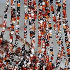 May include: A strand of agate beads in shades of red, orange, white, and black. The beads are faceted and have a natural, irregular shape.