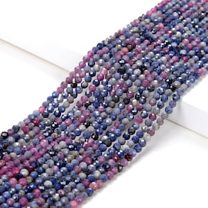 Könnte beinhalten: Eine Strähne facettierter Saphirperlen in Blautönen und Violett. Die Perlen sind klein und rund und auf einer durchsichtigen Schnur aufgefädelt.