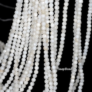 May include: A strand of white iridescent round beads. The beads are made of mother of pearl and have a smooth, polished finish.